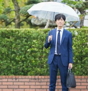 雨の日に傘を差し、黒い就活バッグを持って移動するリクルートスーツ姿の男性