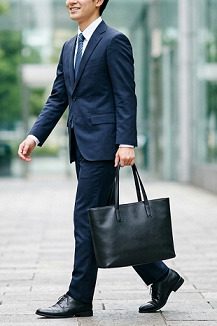 黒のトートバッグを持ち、スーツ姿で歩く就活生の男性