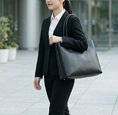 就職活動のスーツ姿で黒のトートバッグを肩に掛けて歩く女性