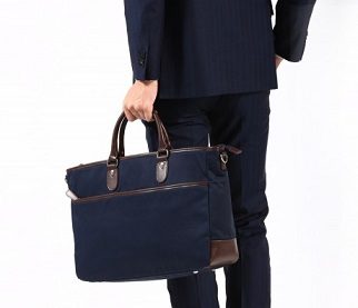 ネイビーのスーツを着て、就活にふさわしいファスナー付きの黒いバッグを手に持つ男性の背面