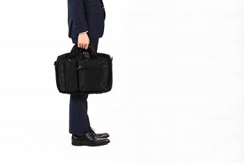 就活シーンをイメージした、手持ちの黒いナイロン製トートバッグとスーツ姿の男性
