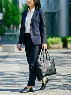 黒のトートバッグを持って歩くスーツ姿の女性の様子