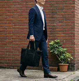黒いトートバッグを持ち、街を歩くスーツ姿の男性